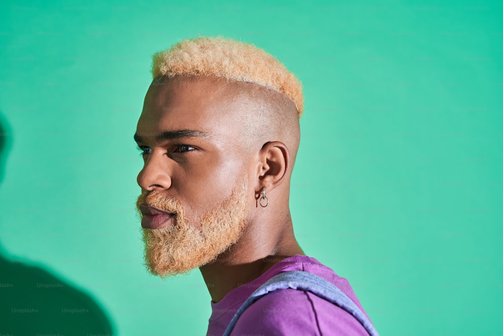 Porträt eines ernsten, gutaussehenden multirassischen Mannes mit blonden Haaren, der wegschaut, während er auf grünem Hintergrund steht. Personen-Erscheinungsbild-Konzept
