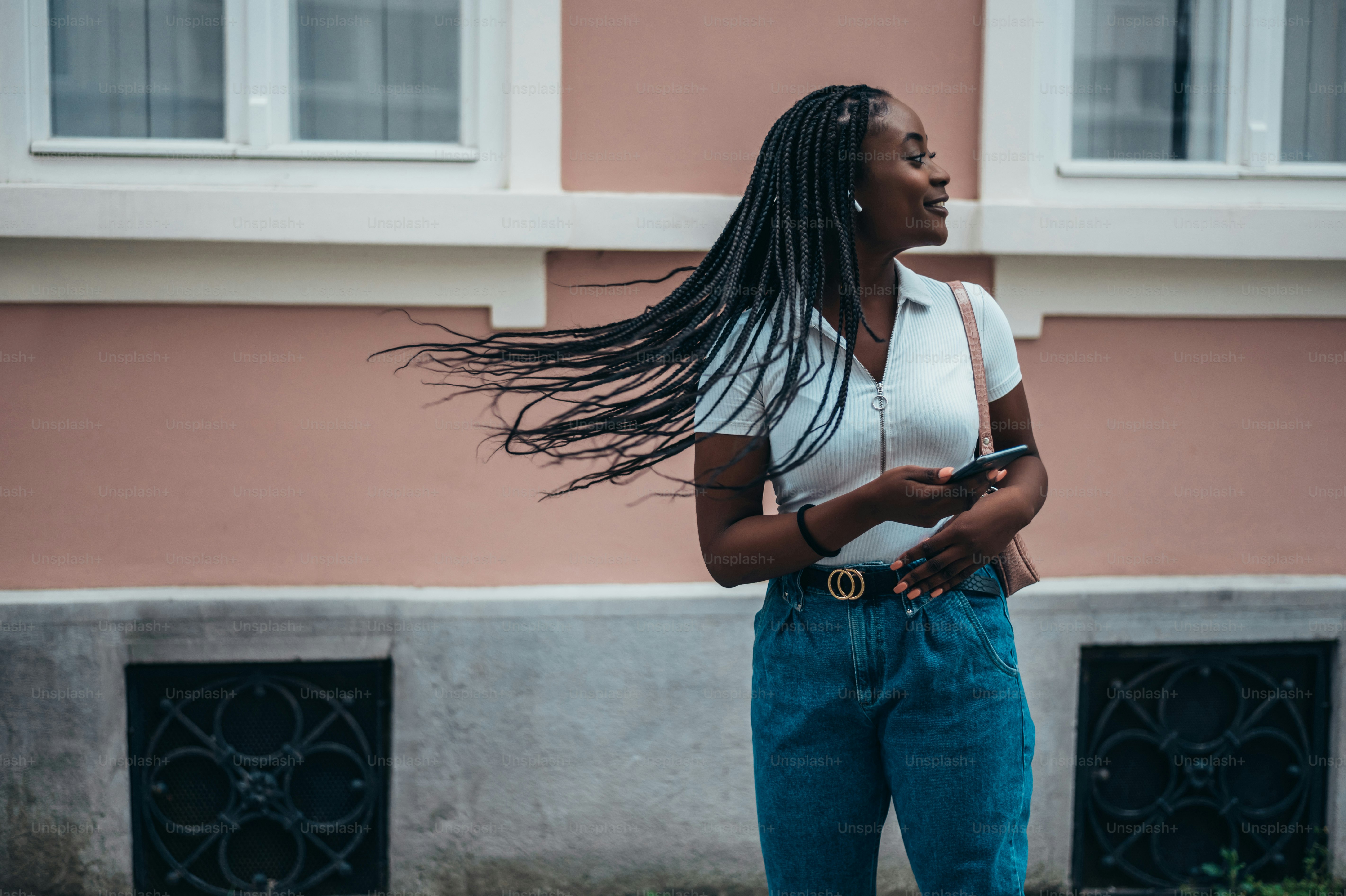 Beautiful african american woman using a smartphone and hair flipping her braids while out in the city by day