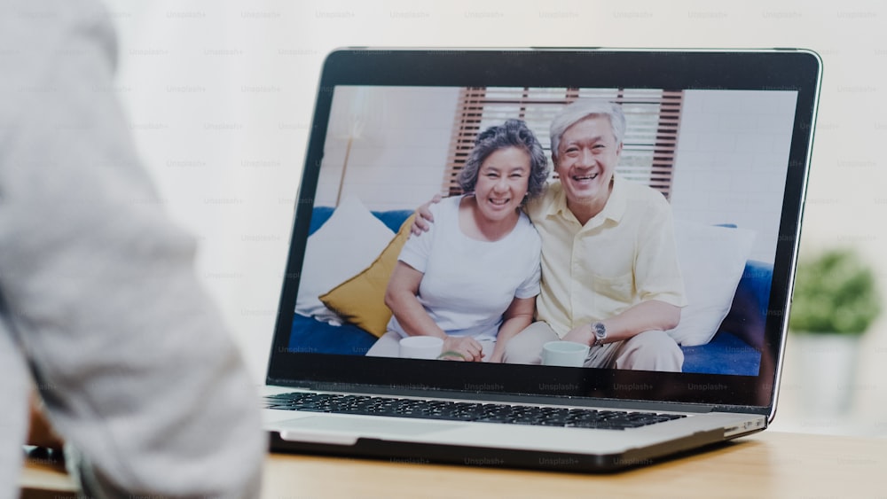 Jovem mulher de negócios asiática usando chamada de vídeo laptop conversando com o pai e a mãe da família enquanto trabalha em casa no quarto de cama. Auto-isolamento, distanciamento social, quarentena para prevenção do coronavírus.