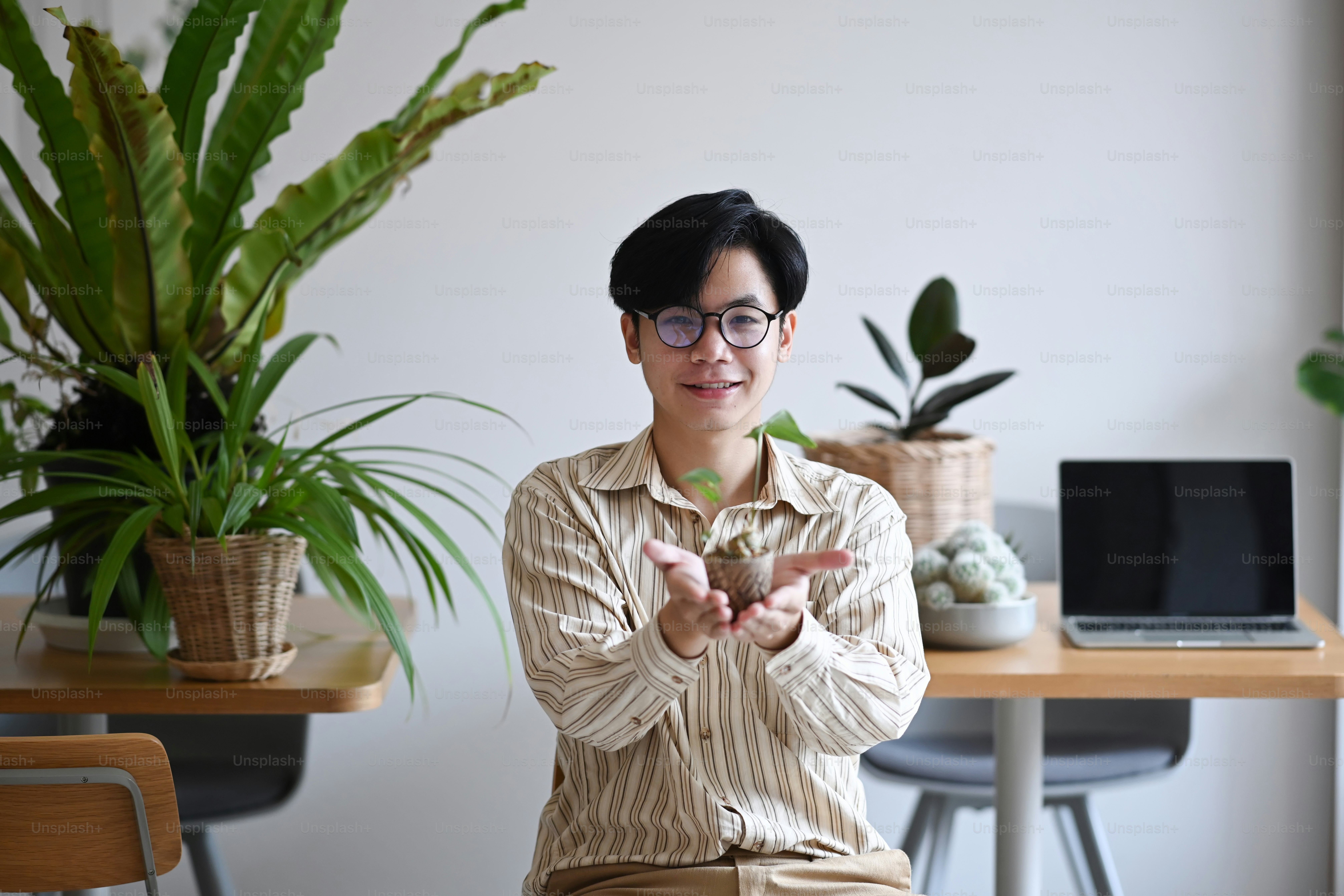 Successful small business entrepreneur sitting in his florist shop and holding small potted plant.