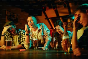 Multi-ethnic group of displeased fans watching sports match on TV in a bar.