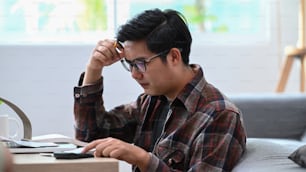 Stressed man using calculator and  managing household finances in living room.