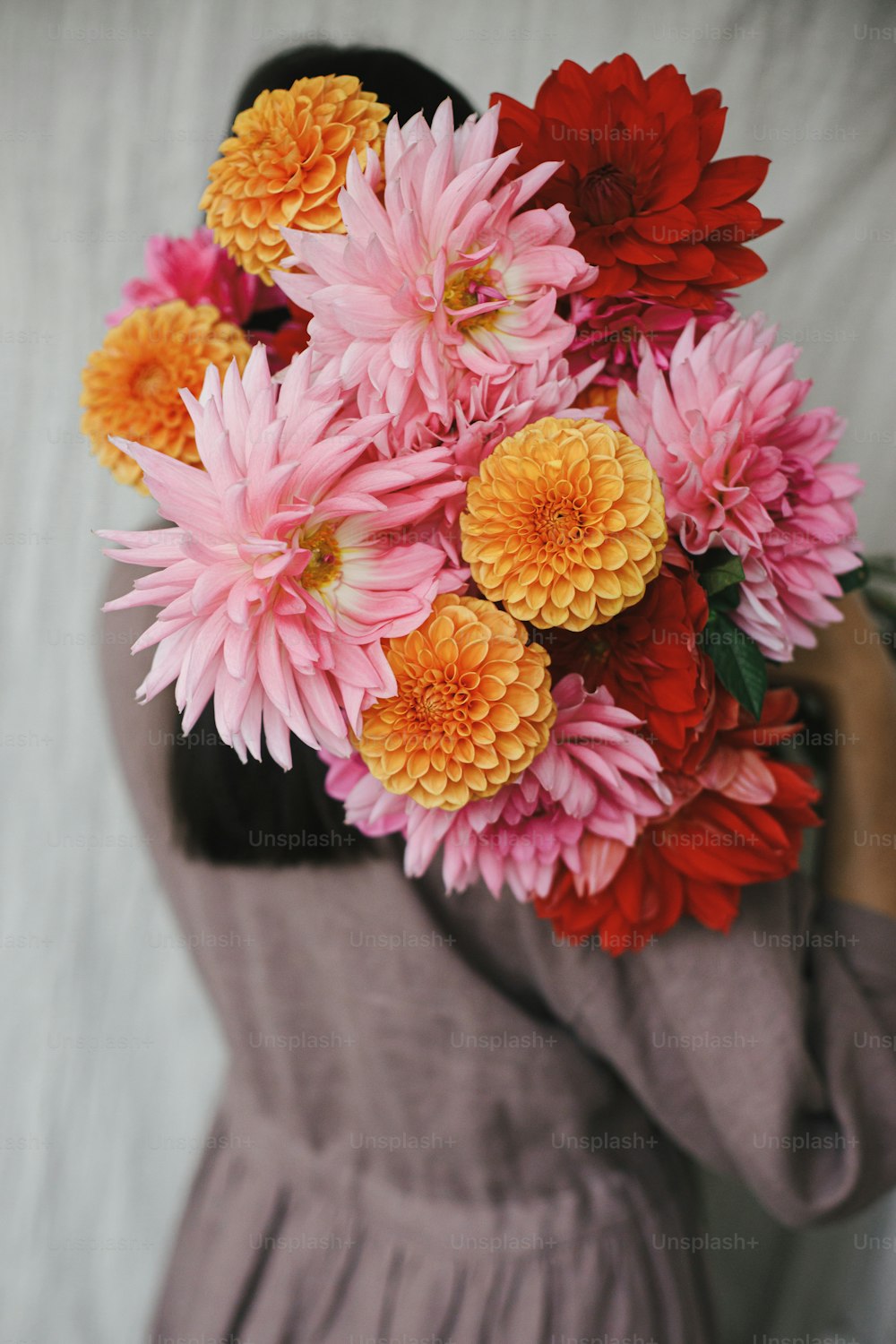 Hermosa mujer sosteniendo el ramo de flores de otoño en habitación rústica. Imagen estética atmosférica. Florista con vestido de lino que se esconde detrás de hermosas dalias de colores. Temporada de otoño en el campo