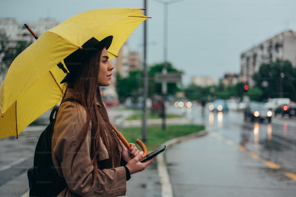 Beautiful young woman using a smartphone and holding yellow umbrella while in the city while it rains