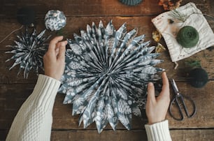 Hände mit stilvollem Weihnachtsstern aus blauem Geschenkpapier auf rustikalem Holztisch flach gelegt. Atmosphärisches stimmungsvolles Bild, nordischer Stil. Handgemachte festliche Dekoration, Urlaubsvorbereitung