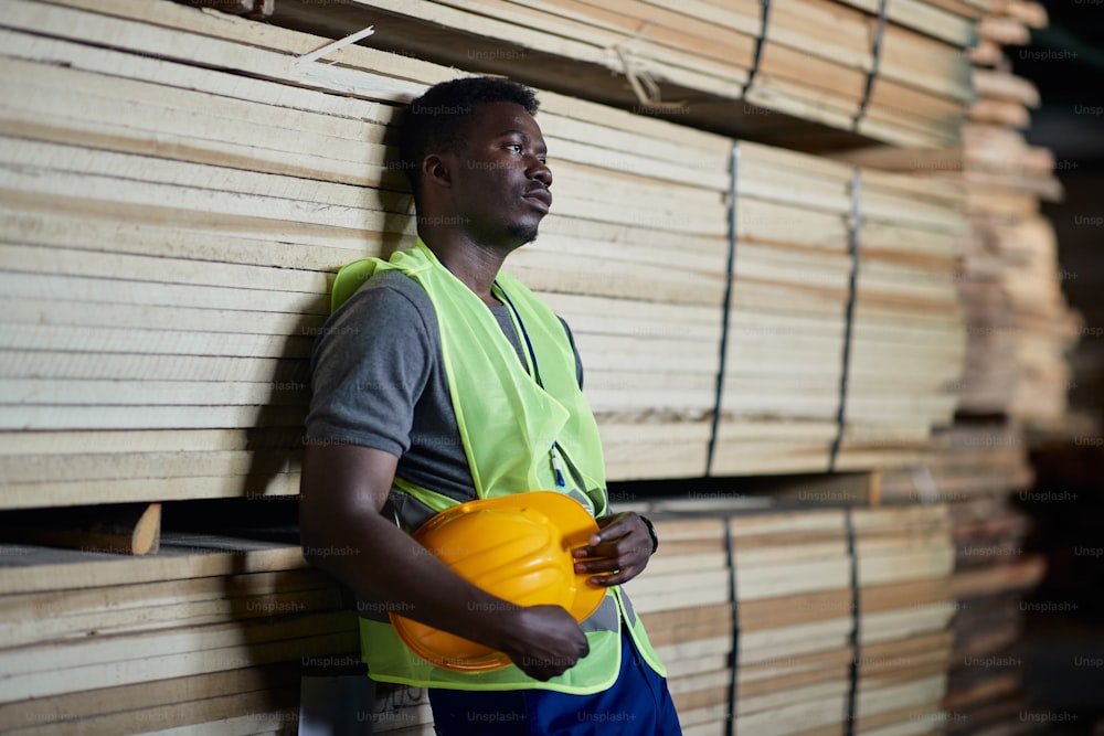Displeased African American worker thinking of something while working at lumber distribution warehouse.