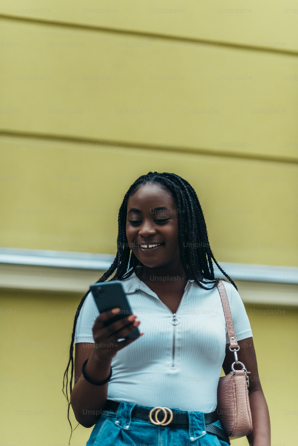 美しいアフリカ系アメリカ人の女性は、街に出かけながらスマートフォンを使用しています