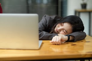 Mujer de negocios joven cansada o agotada durmiendo la siesta en el escritorio de trabajo frente a su computadora portátil en la oficina