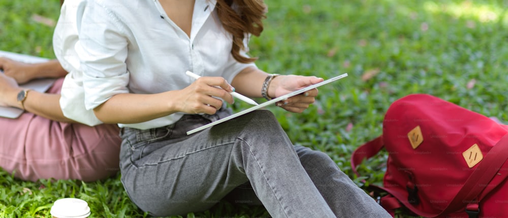 Female graphic designer college students in a park draw a landscape view on a digital graphic tablet computer.