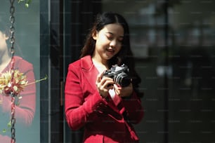 Joven mujer asiática sosteniendo una cámara retro contra la pared de la ventana en la oficina