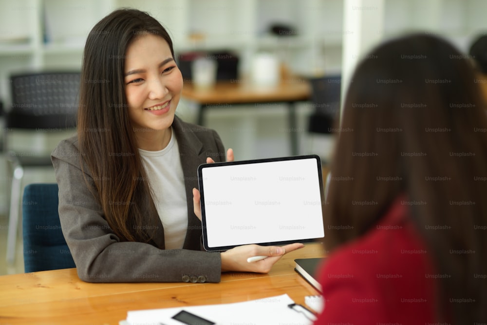 Beautiful insurance broker or agent advising health insurance packages via digital tablet to her client. tablet blank screen mockup