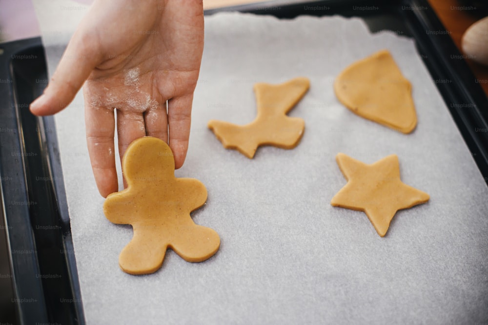 ジンジャーブレッドマンクッキーを他のクリスマス生クッキーと一緒にトレイのベーキングペーパーに手で置きます。不機嫌なイメージ。伝統的なクリスマスジンジャーブレッドクッキーを作る