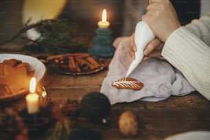 Manos decorando árbol de navidad de galletas de jengibre con glaseado en mesa rústica con servilleta, vela, especias, decoraciones. Imagen atmosférica y cambiante. Hacer galletas de jengibre navideñas tradicionales