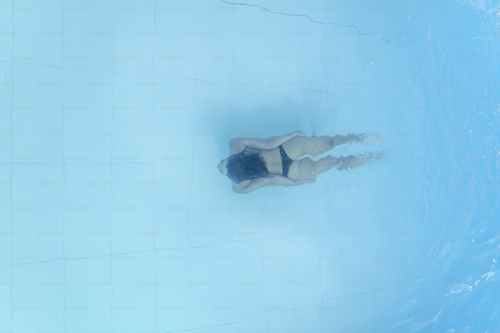 Drohnenansicht auf junge Frau, die im blauen Schwimmbad taucht
