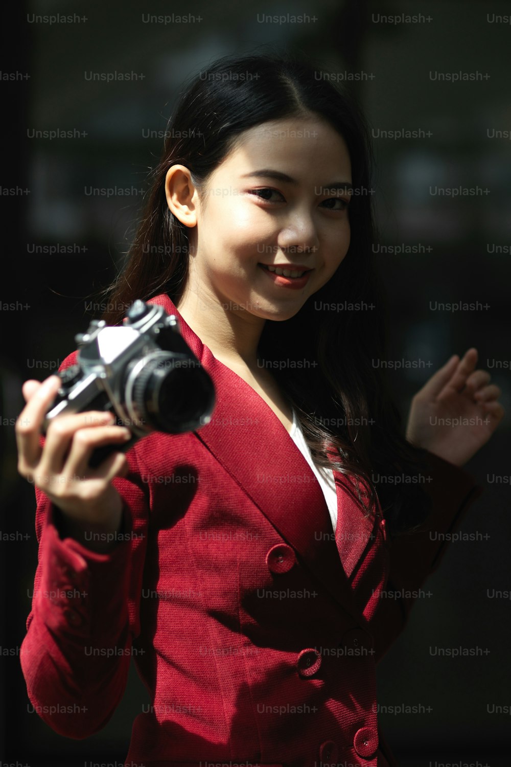 Retrato de una atractiva fotógrafa joven con traje rojo sosteniendo una cámara retro o vintage.