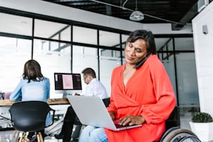 Mexican transgender businesswoman in wheelchair making phone call while working on computer at work in Mexico