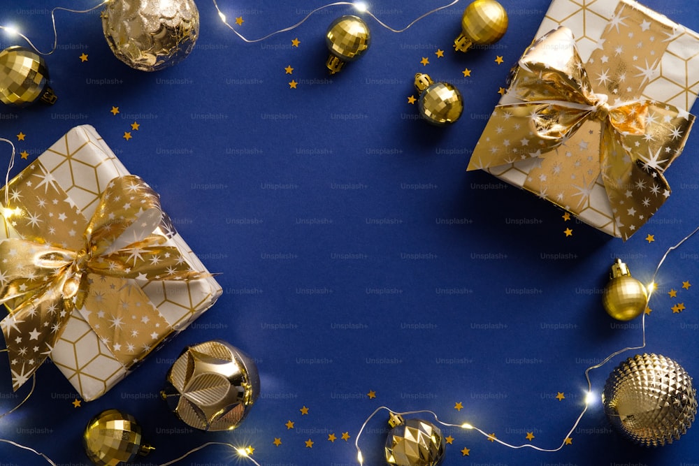 Festive New Year background with golden Christmas decorations, balls, gift boxes on blue. Flat lay, top view. Christmas card design.