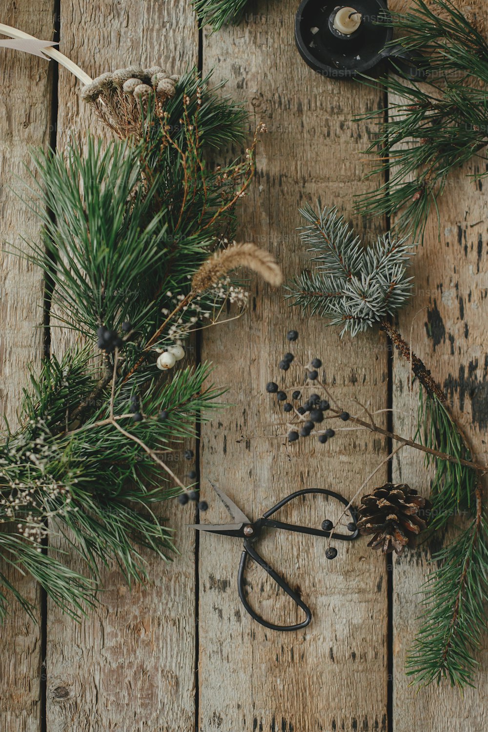 Modern christmas wreath flat lay. Stylish xmas wreath with spruce branches, herbs, scissors,candle, pine cones on rustic wood. Moody image. Merry Christmas! Winter holidays preparation