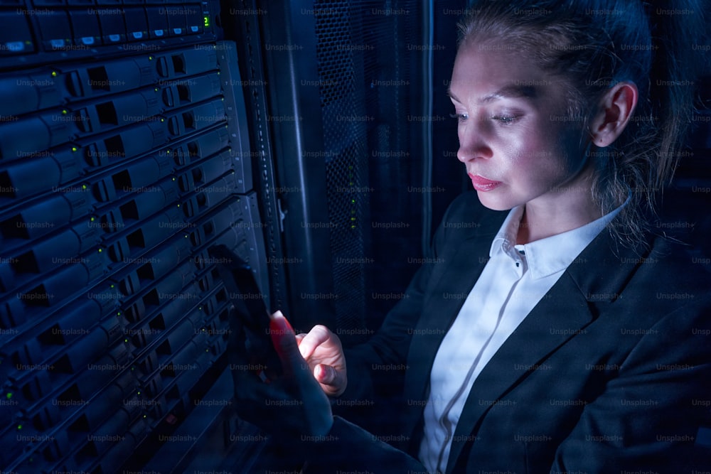 Closeup of female IT engineer using remote equipment while working with supercomputer in data center server room