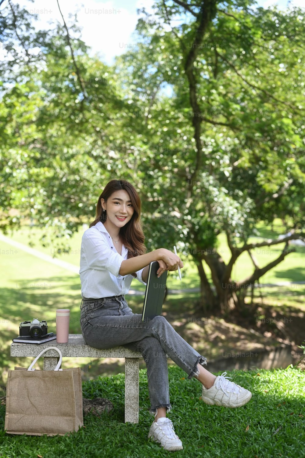Full length portrait of beautiful woman sitting on bench in the park.