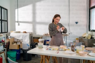 Mujer asiática aprendiendo a pintar el color de su cerámica hecha por ella misma en casa. La confianza femenina disfruta de pasatiempos y actividades de ocio en interiores, artesanía, cerámica, escultura y taller de pintura en el estudio de cerámica.