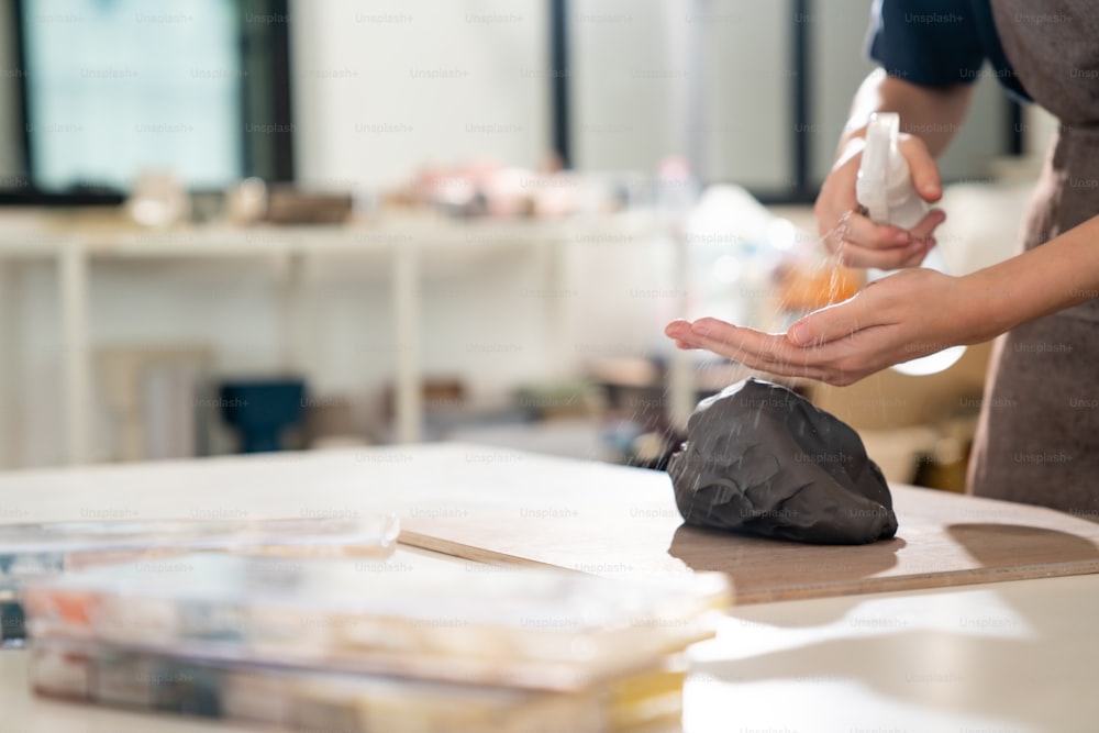 Primo piano delle mani dell'artista scultore donna impasta l'argilla per realizzare sculture in ceramica sul tavolo dello studio di ceramica. Artigiana che prepara l'argilla grezza per lo stampaggio della ceramica in officina. Concetto di prodotto artigianale per piccole imprese.