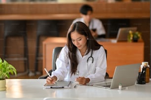 Una giovane dottoressa lavora su una tavoletta digitale. In un ufficio d'ospedale, un medico in camice bianco legge una ricerca di anamnesi passata.