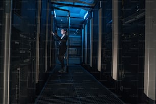 Confident businesswoman holding cellphone and looking at server room in modern data center