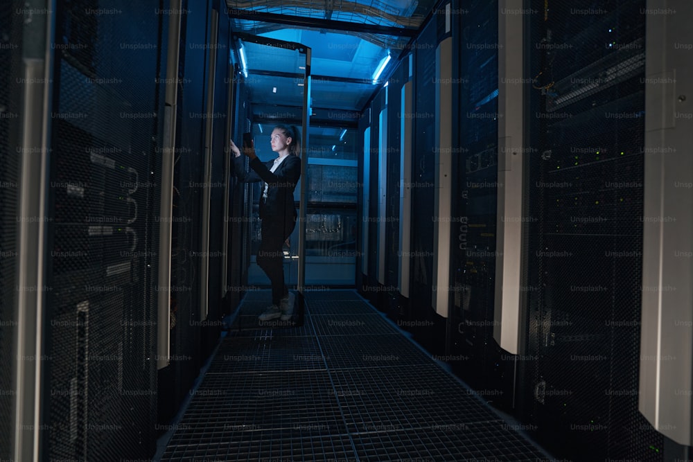 Confident businesswoman holding cellphone and looking at server room in modern data center