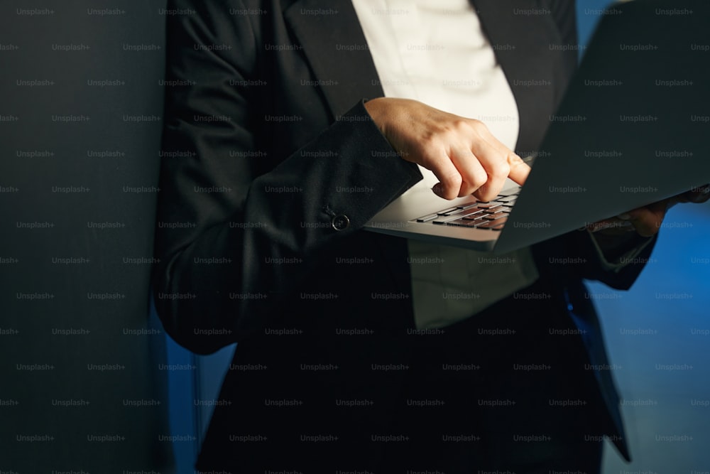 Cropped shot of woman data engineer in black suit holding laptop while working with supercomputer in server room