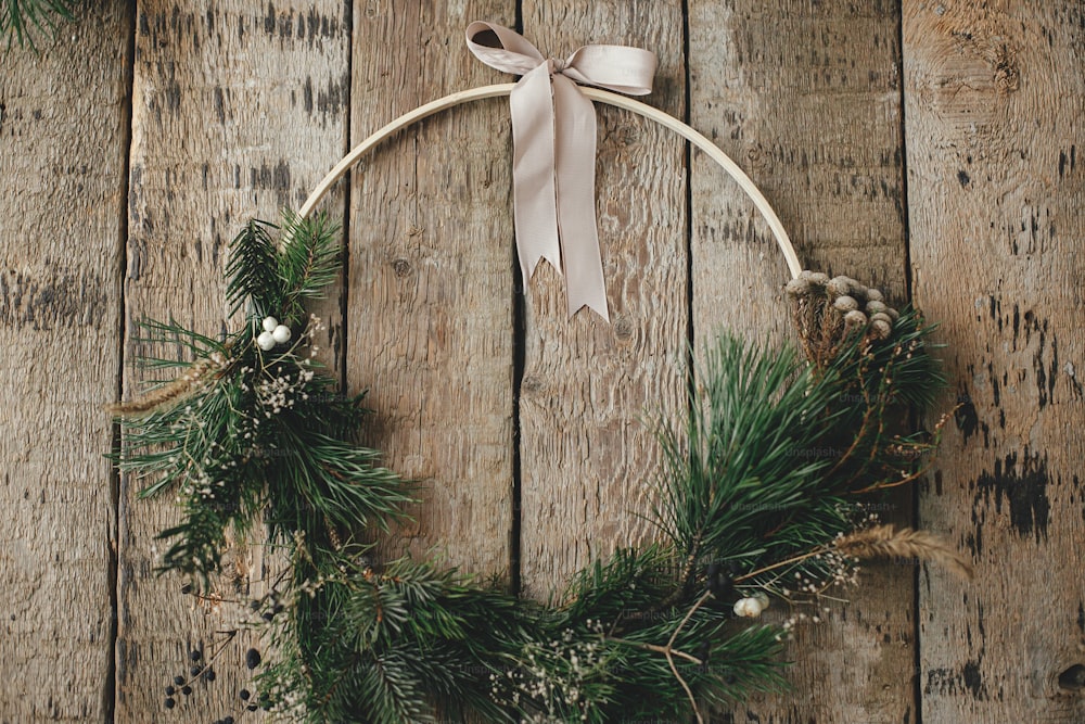 Modern christmas wreath rustic flat lay. Stylish boho xmas wreath with spruce branches, herbs, berries, ribbon on rustic wood. Merry Christmas! Moody image. Seasons greetings