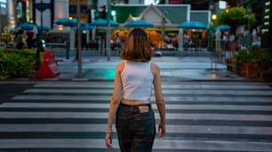 Retrato da jovem mulher asiática bonita andando na faixa de pedestres da rua na cidade e olhando para a multidão de pessoas e luzes noturnas iluminadas. Menina bonita desfrutar de estilo de vida urbano ao ar livre e vida noturna da cidade.