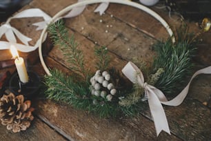Elegante corona navideña moderna sobre mesa de madera rústica con brunia, cintas, vela, hilo, piñas. ¡Feliz Navidad y Felices Fiestas! Preparación para las vacaciones de invierno, imagen atmosférica