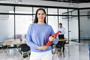 Portrait of young latin businesswoman holding a red folder in meeting with colleagues in modern office in Mexico