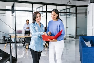 Two young hispanic businesswomen reviewing documents at workplace in Mexico City