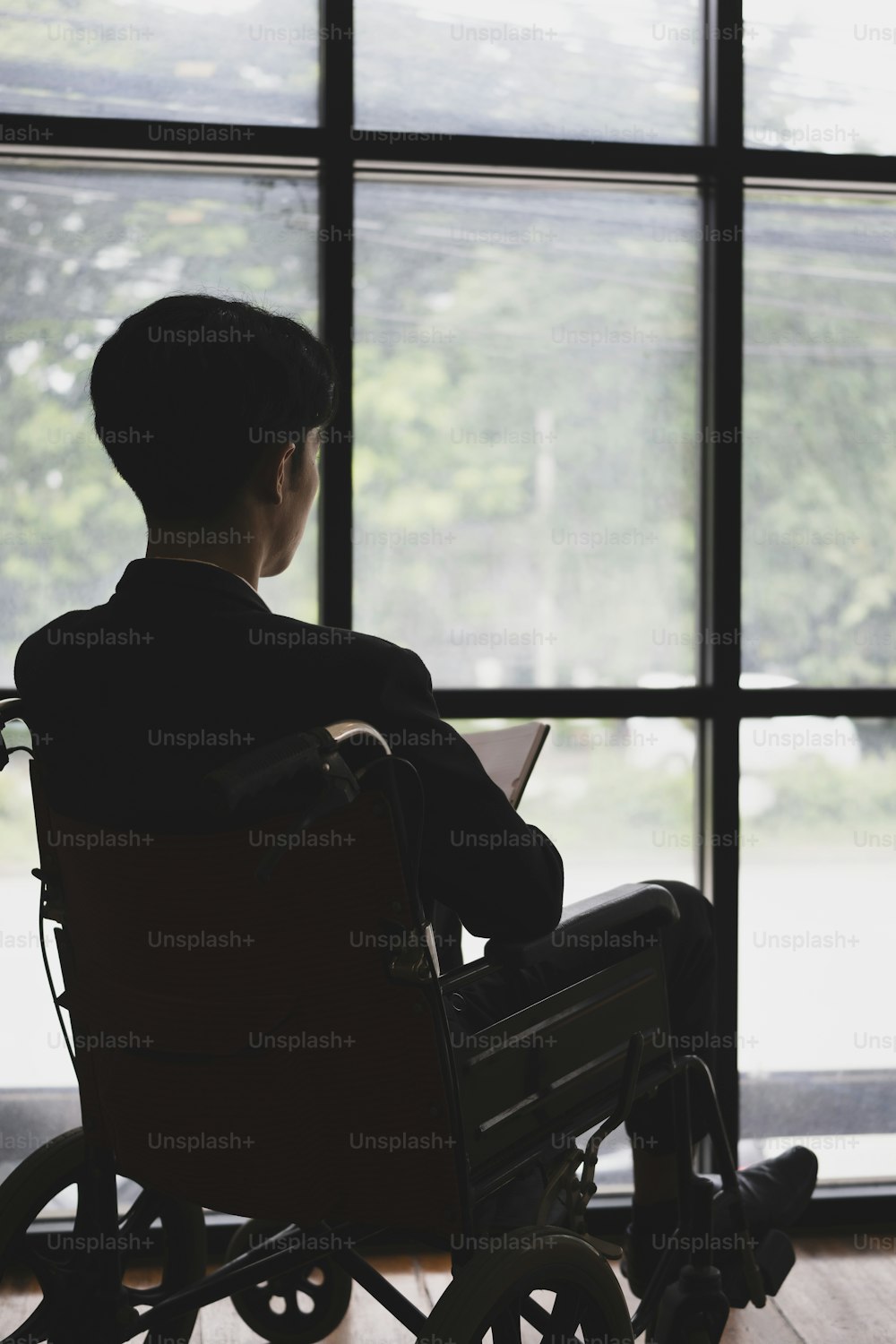 Vista traseira do homem de negócios pensativo em cadeira de rodas sentado na sala de escritório e olhando pela janela.