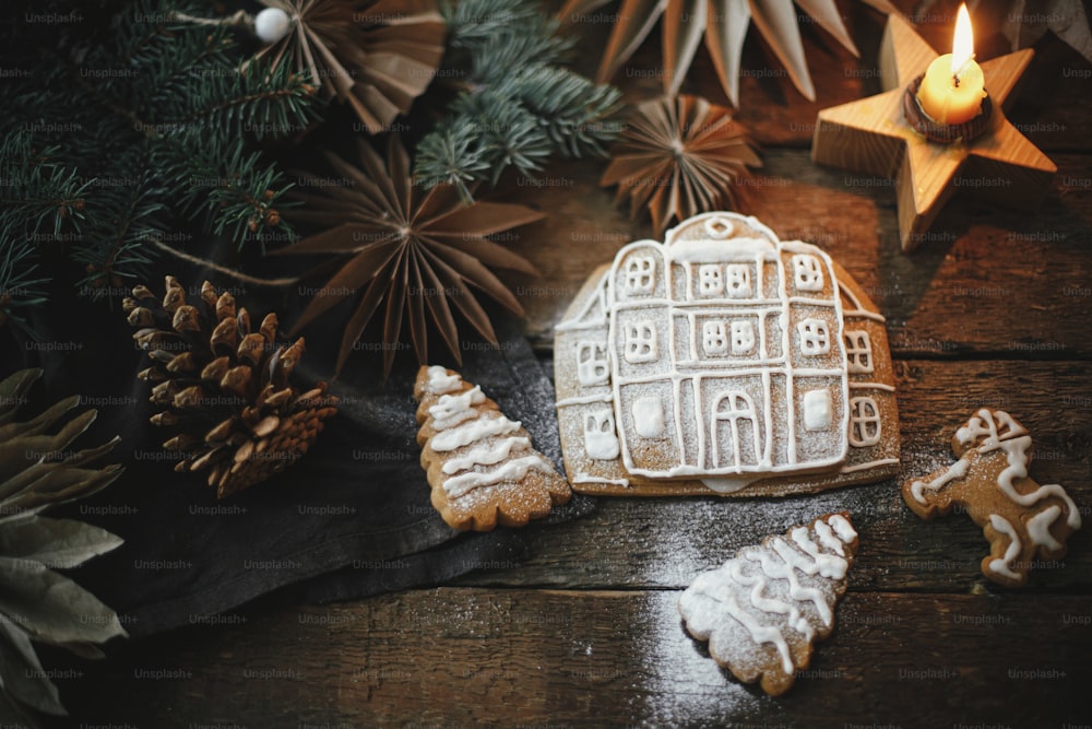 キャンドルとオーナメントのある素朴な木製のテーブルにアイシングを施したクリスマスジンジャーブレッドクッキー、フラットレイ。フロスティングでジンジャーブレッドハウスを作る。雰囲気のあるムーディーなイメージ。メリークリスマス！
