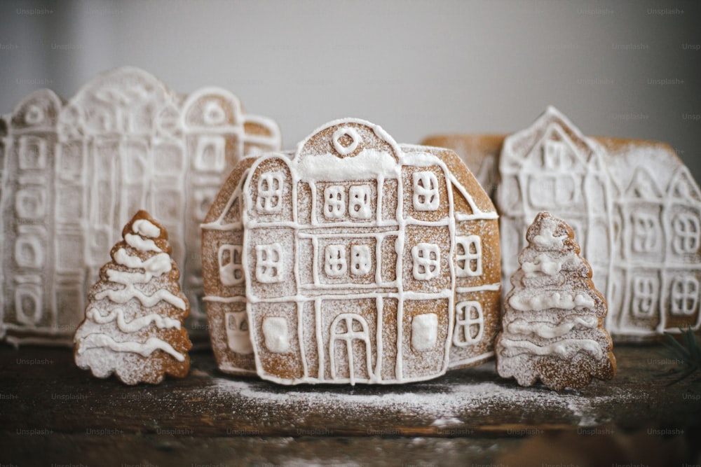 Joyeux Noël! Maisons de Noël en pain d’épice et arbres dans la neige poudreuse sur une table en bois rustique. Image atmosphérique de mauvaise humeur. Scène de village de biscuits de Noël.  Préparation des fêtes et traditions