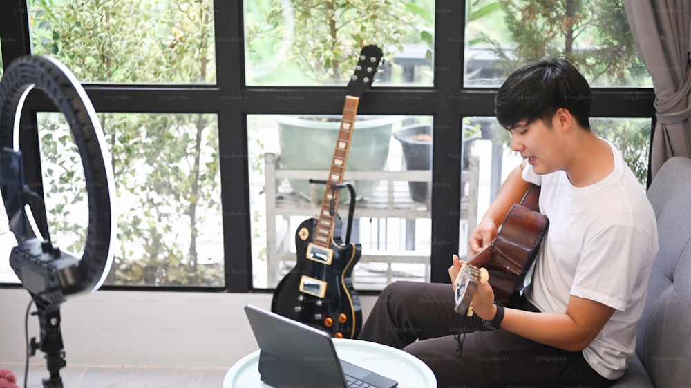 Young male blogger playing guitar and recording video at home.