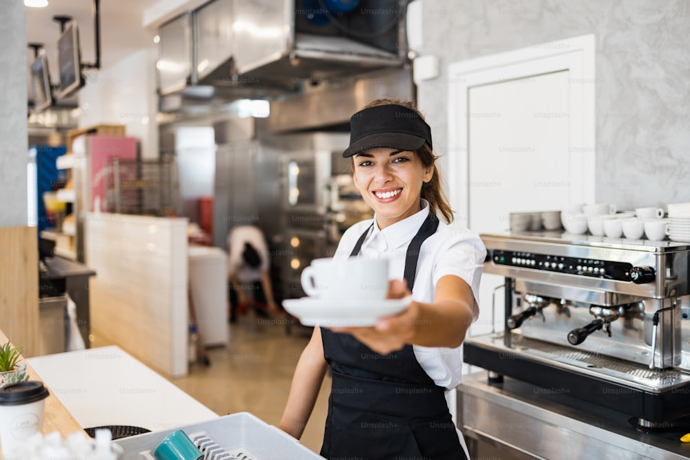 빵집이나 패스트 푸드 레스토랑에서 일하고 커피 머신을 사용하는 아름답고 행복한 젊은 여성 노동자. 중소기업 개념의 긍정적 인 사람들.
