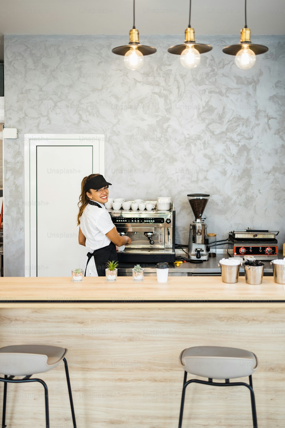 Beautiful and happy young female worker working in a bakery or fast food restaurant and using coffee machine. Positive people in small business concept.