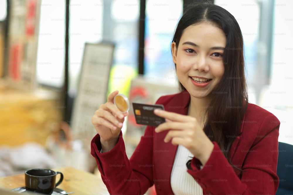 Pretty young businesswoman in red suit holding black credit card in her office, online shopping or internet banking concept.