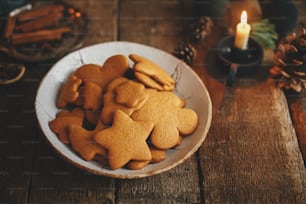 Freshly baked christmas gingerbread cookies in plate on background of rustic table with candle, spices, decorations. Moody image. Making traditional christmas gingerbread cookies. Happy Holidays