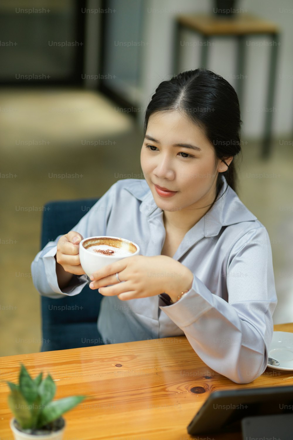 Giovane donna d'affari felice che si gode il suo caffè pomeridiano alla sua scrivania in ufficio.
