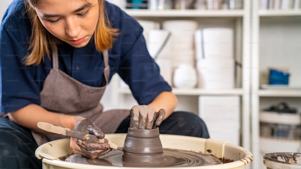 Mulher asiática bonita escultor artista escultura argila na roda de cerâmica no estúdio de cerâmica. Artesão fêmea moldando argila crua criar formas de cerâmica na oficina. Conceito de produto artesanal para pequenas empresas.