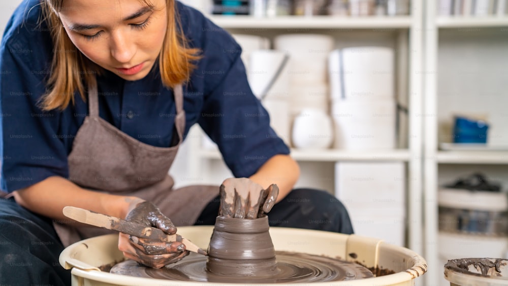 Bella donna asiatica scultrice artista scultura argilla su tornio di ceramica presso studio di ceramica. L'artigiana che modella l'argilla grezza crea forme di ceramica in laboratorio. Concetto di prodotto artigianale per piccole imprese.