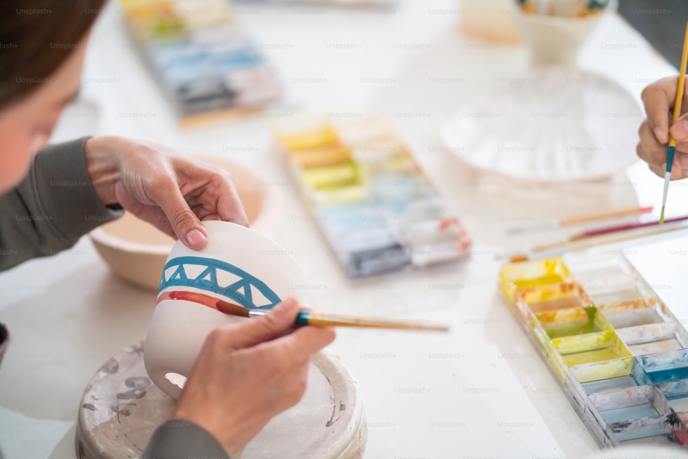 Un gruppo di amici asiatici della generazione millenaria si diverte e si diverte a dipingere insieme ceramiche autoprodotte presso lo studio di ceramica. Hobby e attività ricreative al chiuso, laboratorio di pittura su ceramica fatta a mano.