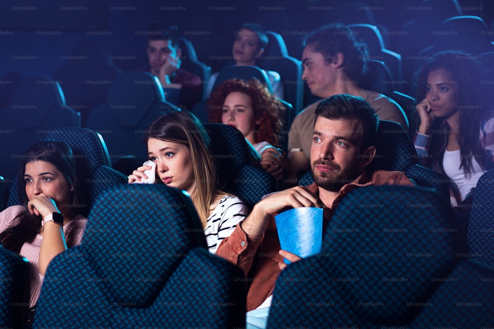 Grupo de pessoas assistindo filme triste no cinema.