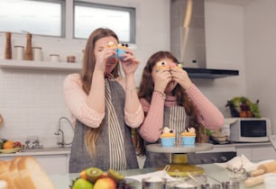 Happy family concept of a mother and her daughter enjoying cupcakes together in the kitchen at home.