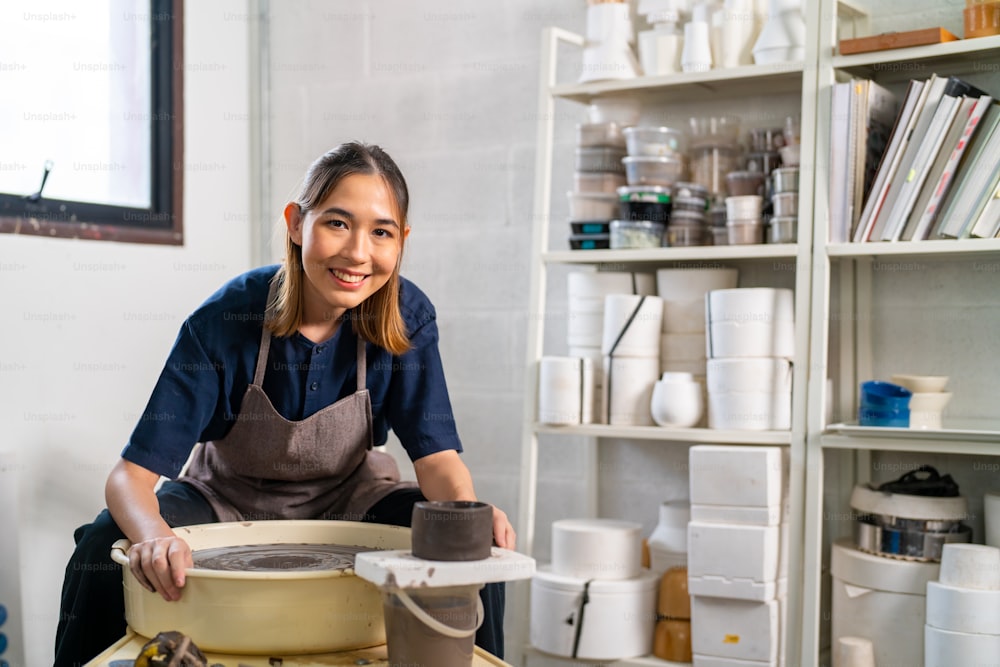 Portrait of Beautiful Asian woman sculptor artist sculpture clay on pottery wheel at ceramic studio. Female craftsman molding raw clay create pottery shapes at workshop. Small business handicraft product concept.